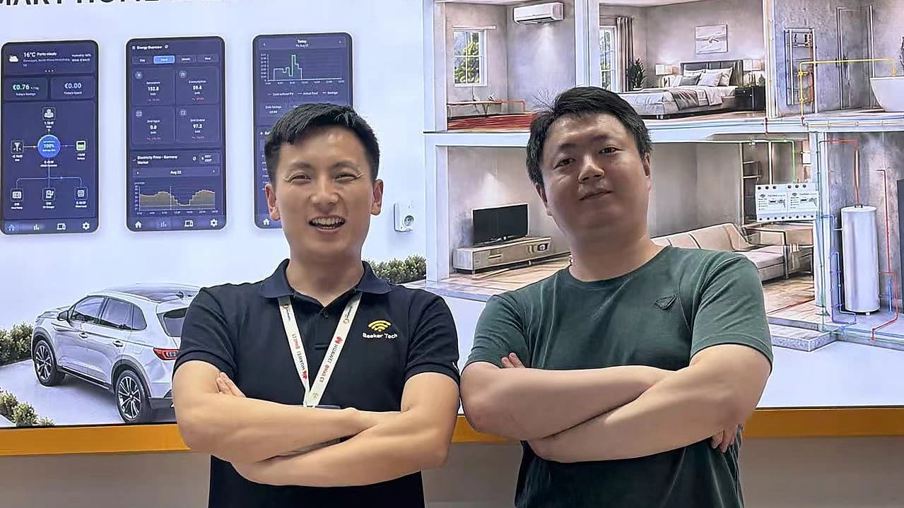 Two members of the OptiBee team on the OptiBee stand at an energy trade fair, in front of the home energy display.